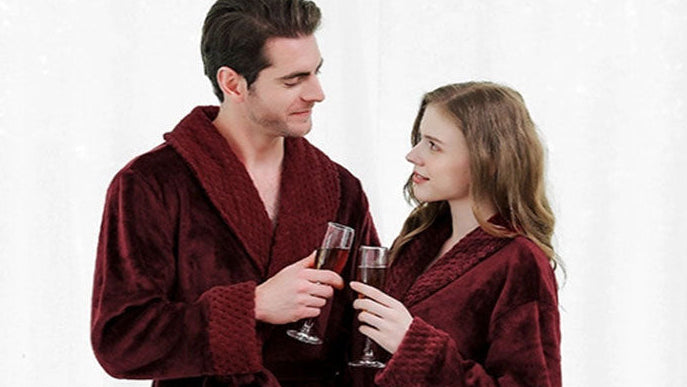 Man and woman in burgundy robes holding drinks against a white curtain background